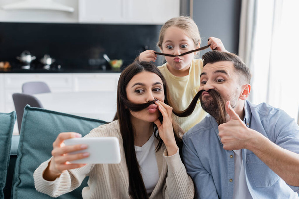 woman taking selfie with family having fun while imitating mustache with her hair - Foto, afbeelding