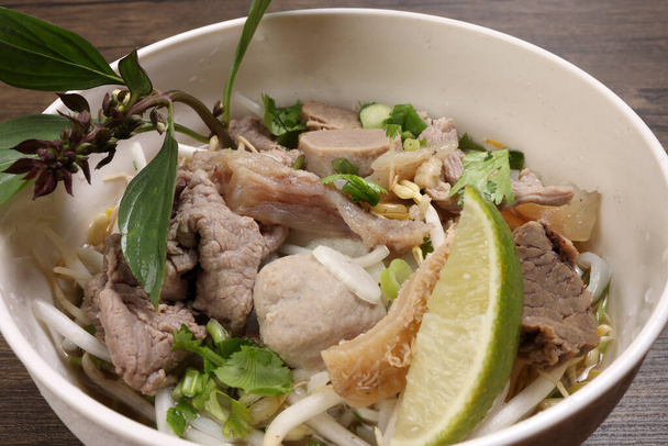Vietnamesisch Poh Rindfleisch Nudeln Suppe Brühe mit Rindfleischbällchen Brustkutteln Magen Teile wurden gekeimt Thai-Basilikum-Limette in Schüssel auf Holztisch - Foto, Bild