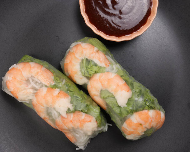 Camarones gambas vietnamitas ver a través de papel de arroz rollo de primavera salsa vegetal verde en plato oscuro - Foto, imagen