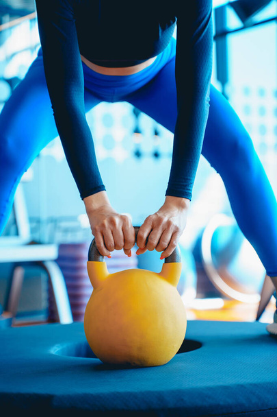 Girl in sportswear lifts a heavy yellow kettlebell, standing on the platform, fitness gym - Foto, immagini