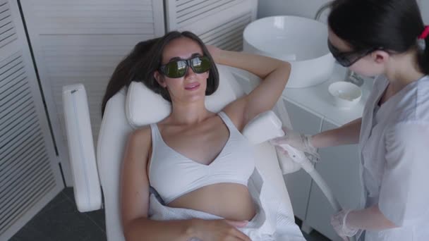 beautician doing armpit laser hair removal of attractive sexy woman lying on medical couch and smiles in beauty salon. Cosmetologist does laser hair removal of armpits of patient. Epilation procedure - Video
