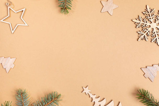 Christmas or New Year beige background with frame of wooden festive decorations - Xmas toys and fir tree twigs with copy space in center. Top view. Horizontal orientation. - Fotografie, Obrázek