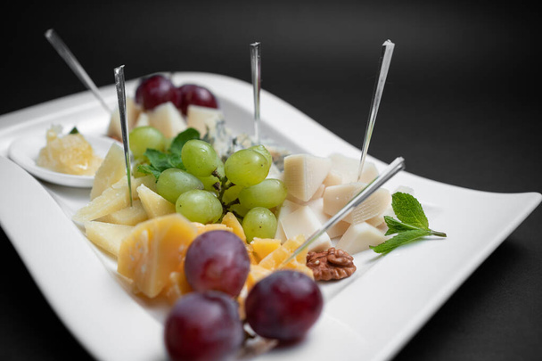 closeup of cheese plate with grape, walnuts and honey on black background - Foto, Imagen