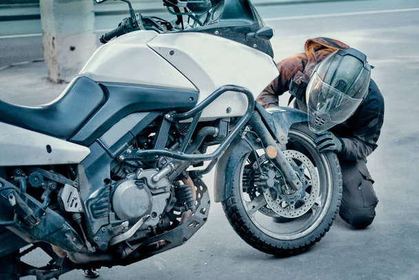 A bukósisakos motoros ellenőrzi a motorkerékpárja kerekének sérülését. - Fotó, kép