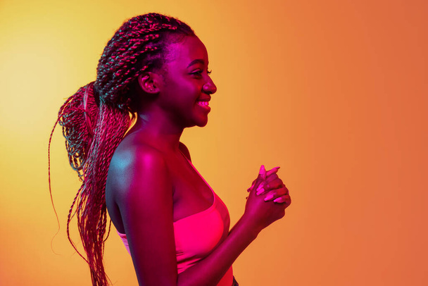 Joyful young beautiful African girl, female fashion model isolated on yellow background in neon. Concept of human emotion, facial expression. - Foto, imagen