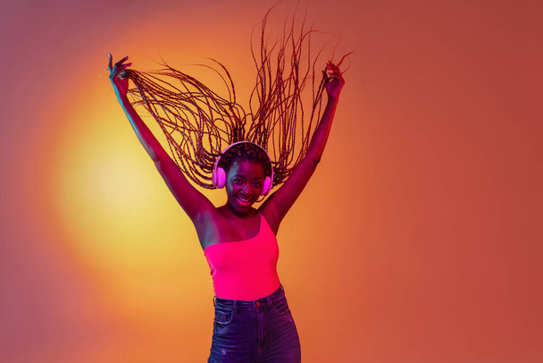 Joyful young beautiful African girl, female fashion model isolated on yellow background in neon light. - Foto, immagini