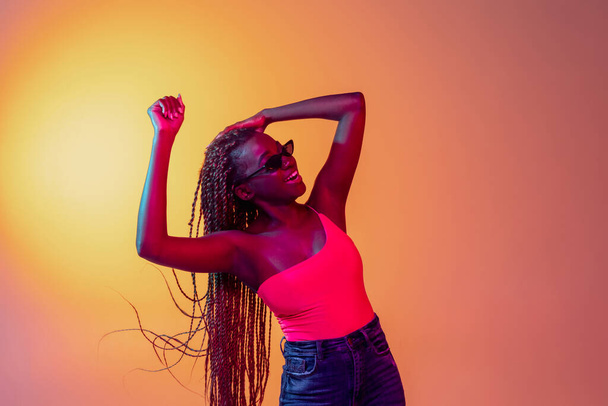 Gioioso giovane bella ragazza africana, modello femminile isolato su sfondo giallo in luce al neon. - Foto, immagini