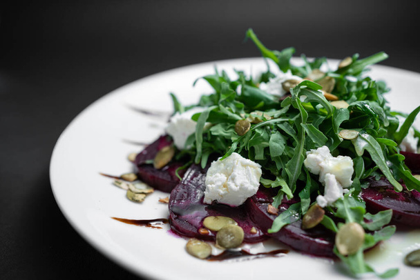 closeup of salad with beet, arugula and feta cheese on plate on black background - Fotografie, Obrázek