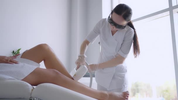 Epilación láser. Mujer recibiendo procedimiento de depilación láser en sus piernas. Salón de belleza tratamiento láser clínica cosmetología esteticista profesión profesional cuidado corporal concepto - Imágenes, Vídeo