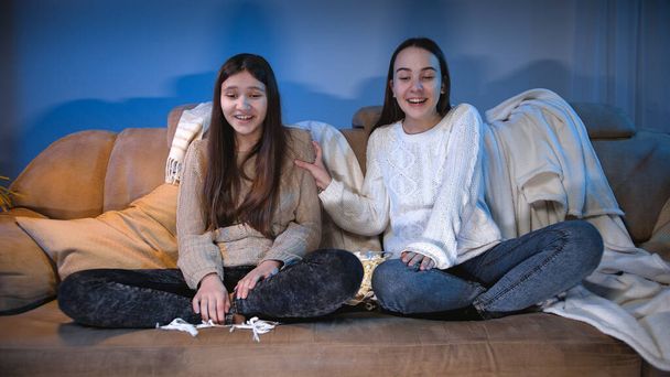 Twee vrolijke vrolijke meisjes lachen en plezier hebben tijdens het kijken naar comedy film 's nachts - Foto, afbeelding