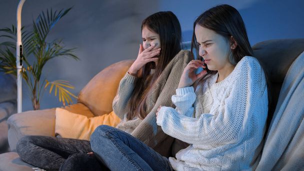 Kaksi tyttöä sulkevat silmänsä ja kääntyvät pois katsoessaan inhottavaa tai kurjaa ohjelmaa televisiosta - Valokuva, kuva