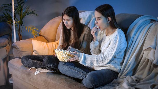 Přátelé jíst popcorn z velké misky při sledování TV show v obývacím pokoji v noci - Fotografie, Obrázek