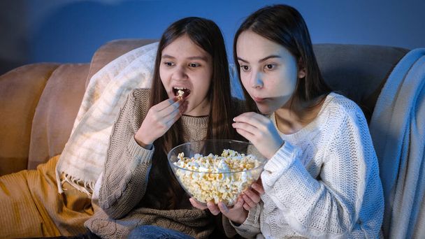 Щасливі усміхнені дівчата насолоджуються переглядом телевізійного шоу та їдять попкорн вночі
 - Фото, зображення