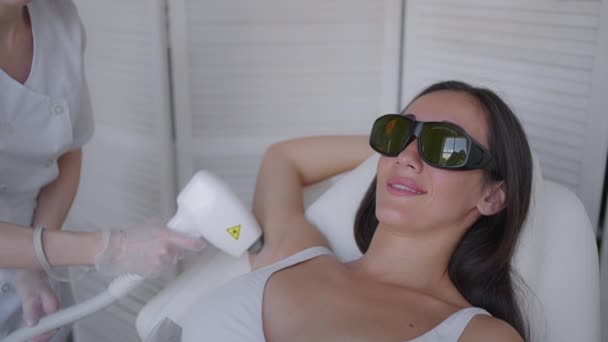 estetista facendo ascella depilazione laser di attraente donna sexy sdraiata sul divano medico e sorride nel salone di bellezza. Il cosmetologo fa la depilazione laser di ascelle di paziente. Procedura di pilotaggio - Filmati, video