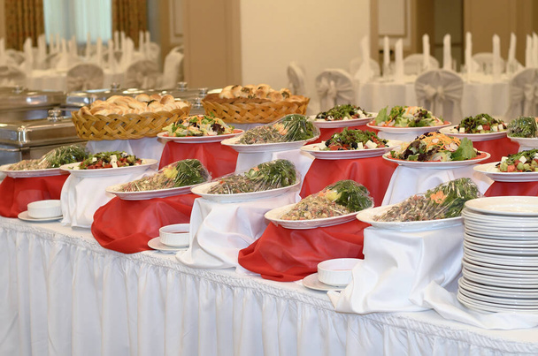 Catering spoustu salátů ze zeleniny a masa na bílém a červeném ubrusu ve velké hodovní síni - Fotografie, Obrázek