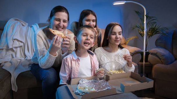Glückliche Familie lächelt und lacht, während sie Pizza isst und abends Fernsehfilme oder Serien guckt. - Foto, Bild