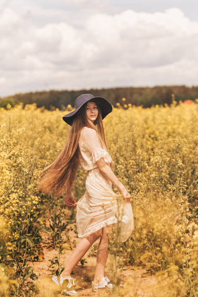 A young happy girl enjoys nature on the field of blossoming canola. The corcept of youth and freedom. Vertical - Photo, Image