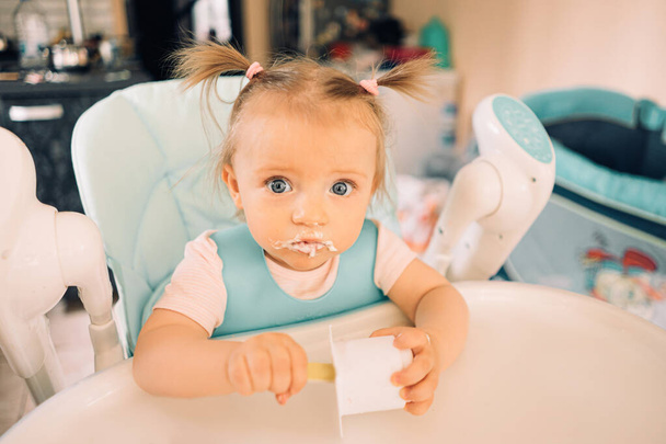 Děvče v kuchyni u stolu na dětské židličce jí jogurt - Fotografie, Obrázek