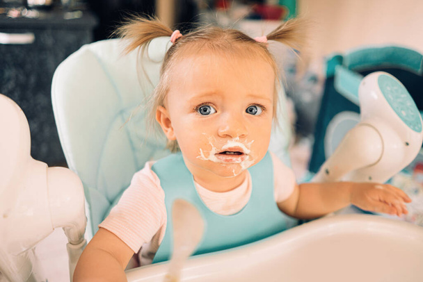 Niña en la cocina en la mesa en la silla de un niño comiendo yogur - Foto, imagen