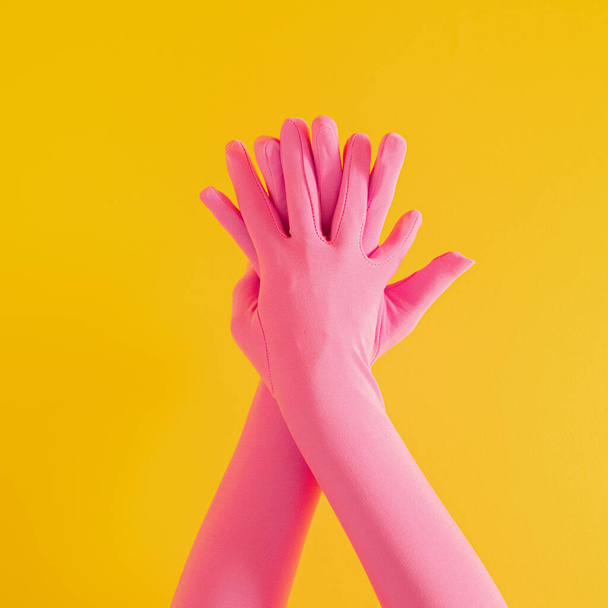 hands with pink glove on yellow sunny summer background. modern summer abstract art. mimalism - Фото, изображение
