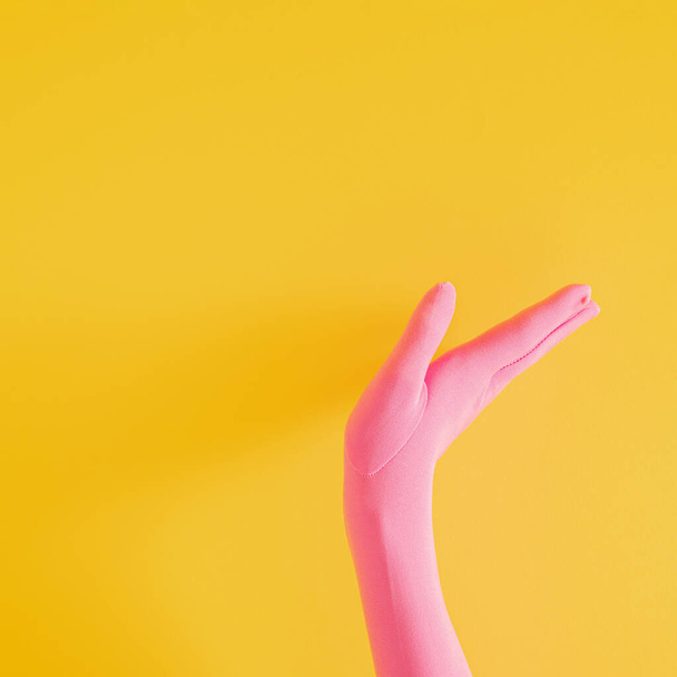 handen met roze handschoen op gele zonnige zomerachtergrond. moderne zomer abstracte kunst. mimalisme - Foto, afbeelding