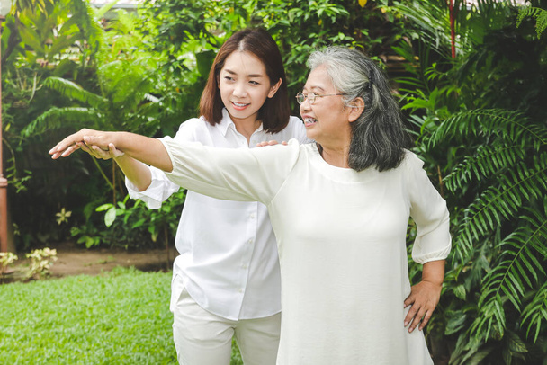 Fizik tedavi gören Asyalı yaşlı kadının kollarını esnetmede yardımcı olacak bir kızı var. İkisi de evin önündeki bahçedeydi. Yaşlılara bakmanın sağlıklı olması kavramı - Fotoğraf, Görsel