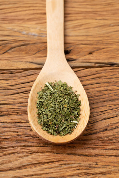 Closeup of dried parsley on a spoon over wooden table. - Foto, afbeelding