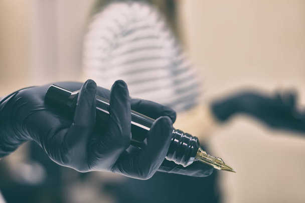 Hand in black gloves holding tattoo machine.  Art and design concept. Close up - 写真・画像