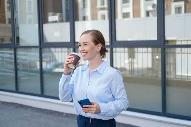 happy confident business woman typing on phone drinking coffee stand in city  - Foto, Imagem