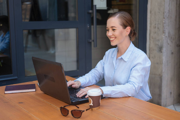 Retrato de mujer joven de negocios feliz, sonriendo mientras está sentado en la caffe y el trabajo con el ordenador portátil - Foto, Imagen