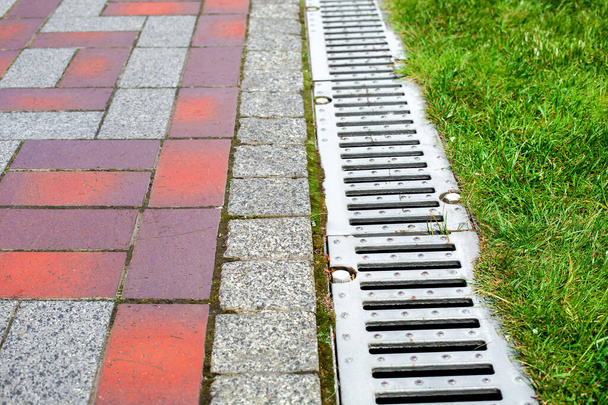 grating of the drainage system for drainage of rainwater in the park at the edge of the sidewalk from a stone slab with a green lawn, landscaping a city garden close-up, nobody. - Photo, image