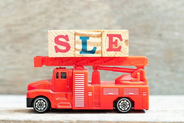 Вантажівка з пожежною драбиною тримає блок літер у слові SLE (Збереження системного вовчака) на фоні деревини
 - Фото, зображення