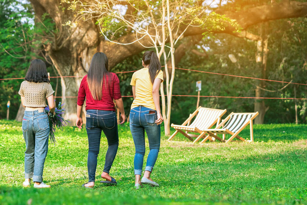 Vue arrière de la femme asiatique avec des amis marchant ensemble sur la pelouse à travers le jardin verdoyant. Les amis du bonheur passent du temps ensemble dehors dans la nature verte. Profiter de la nature en plein air. - Photo, image