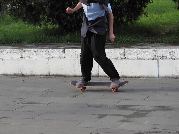 Um menino está montando um skate ao longo de um passeio de granito em um dia de verão - Foto, Imagem