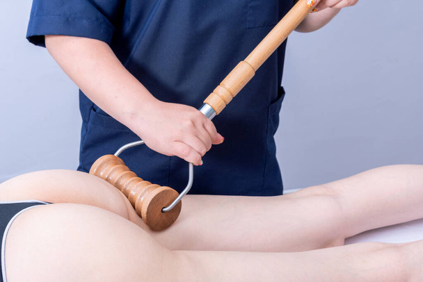 woman having spa massage of the back of the thigh in a beauty salon using a wooden roller massager - Foto, Imagem