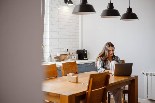 Boldog gyönyörű nő dolgozik laptop, miközben ül az asztalnál otthon - Fotó, kép