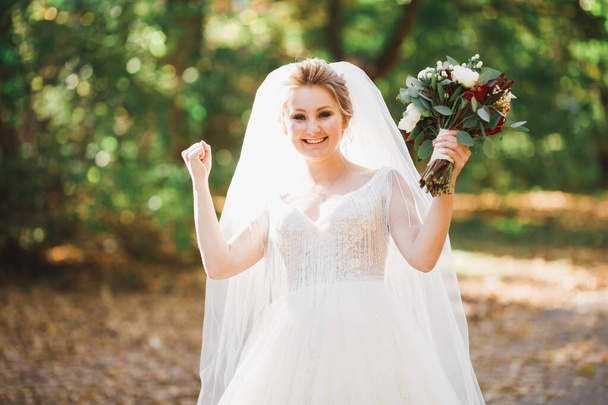 Роскошная свадебная невеста, девушка позирует и улыбается с букетом - Фото, изображение