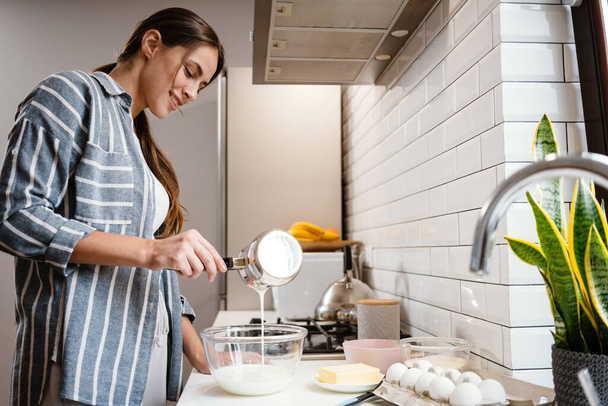 Pleased beautiful woman smiling and making pancake dough at home kitchen - Valokuva, kuva