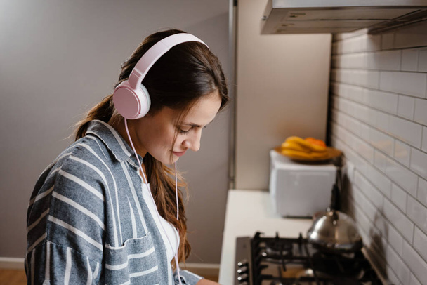 Pleased beautiful woman listening music with headphones at home kitchen - Foto, Imagen
