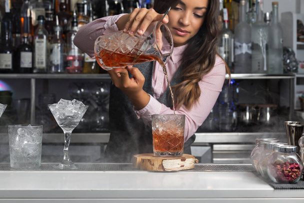 Опытная молодая женщина-бармен наливает коктейль в стакан, подавая напитки на заказ в баре - Фото, изображение