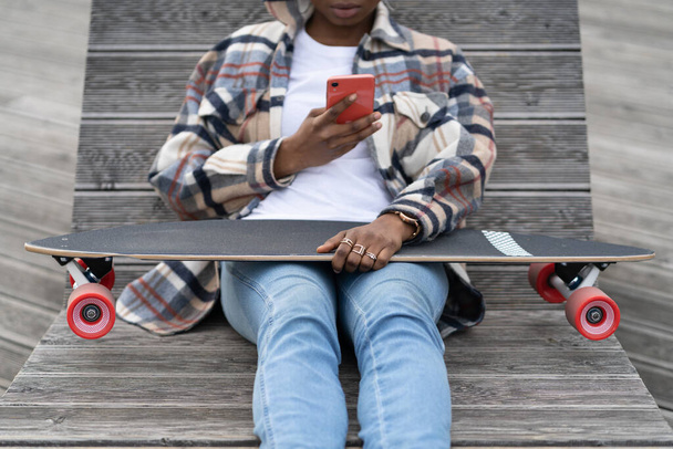 Young african girl sit with skate, chat in mobile phone. Closeup of black skater woman messaging - Foto, Imagem