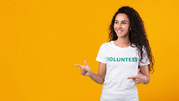 Female Volunteer Pointing Fingers Aside Showing Copy Space, Yellow Background - Foto, immagini