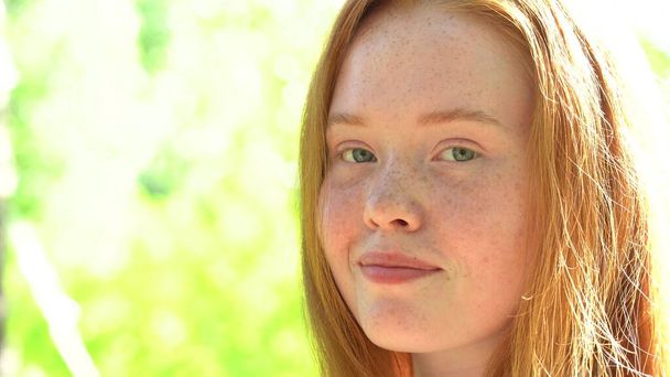 Portrait a smiling young woman with red hair and freckles against the backdrop of a bright sunny meadow. Natural beauty with freckles - 写真・画像