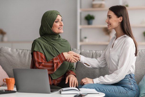 Зрелая мусульманская предпринимательница пожимает руку молодой женщине в офисе - Фото, изображение