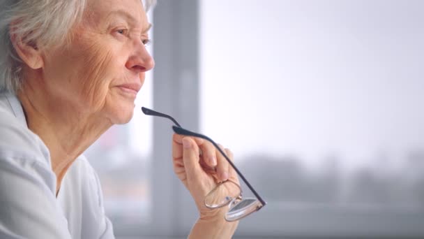 Προσεκτική ηλικιωμένη γυναίκα σε μπλε μπλούζα κρατά σχεδιασμένα γυαλιά - Πλάνα, βίντεο