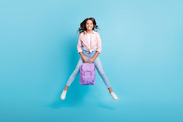 Full size photo of young cheerful good mood positive girl jumping hold purple backpack isolated on blue color background - Foto, afbeelding