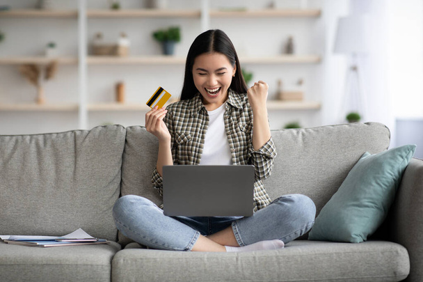 Емоційна жінка використовує ноутбук і кредитну картку вдома
 - Фото, зображення