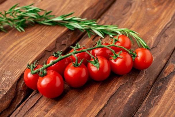 Tomates cherry y romero sobre fondo de madera. Rama de tomate fresco. Comida vegetariana. - Foto, Imagen