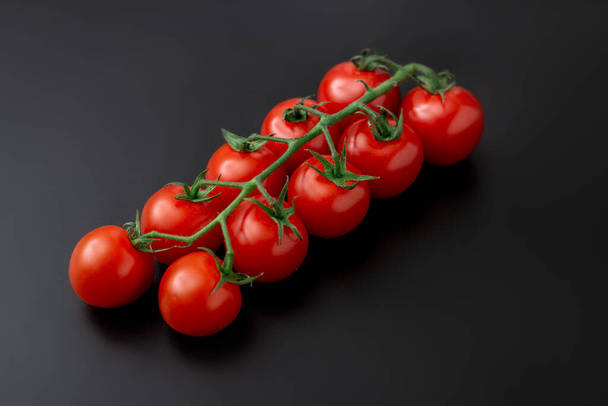 Cherry tomatoes and rosemary on a black background. Fresh tomato branch. Vegetarian food. - Fotó, kép