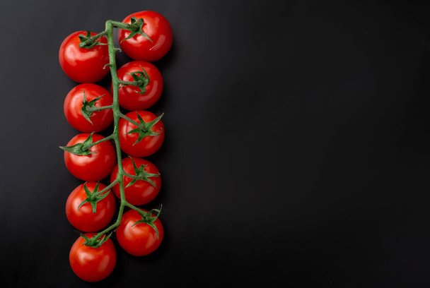 Cherry tomatoes and rosemary on a black background. Fresh tomato branch. Vegetarian food. - Foto, Bild